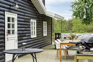 Een blokhut met een veranda, een ronde tafel, stoelen en een barbecue.