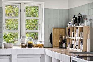 Una cocina con ventana, una planta en maceta y un estante de madera con utensilios de cocina.