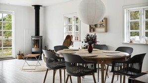 A dining area with a round table, black chairs, a white hanging light, and a wood-burning stove.