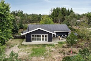 Una casa de dos pisos con garaje, rodeada de un bosque frondoso.