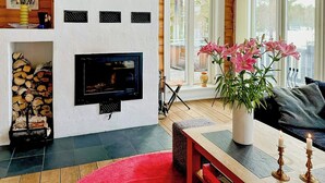 A cozy living room with a fireplace, a television, a red rug, and a large window with a view of trees.