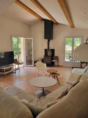 Ein Wohnzimmer mit Fernseher, einer Couch, Sesseln, einem Kamin und einem großen Fenster.