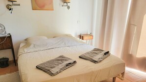 Una cama bien hecha con dos toallas dobladas, una mesita de noche con una lámpara y una lámpara de pared.