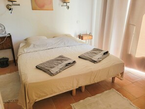 Ein ordentlich bezogenes Bett mit zwei gefalteten Handtüchern, ein Nachttisch mit einer Lampe und einer Wandleuchte.
