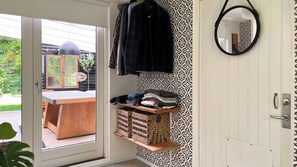 Ein Zimmer mit einer Schiebetür aus Glas, die zu einem Außenbereich führt, einer Holzbank, einem Korbwäscher und einem an der Wand befestigten Spiegel.