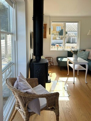 A cozy room with a large black wood stove, wicker furniture, a white table, and a view through a window. - Holiday home by the water in Øer Maritime (Ebeltoft)