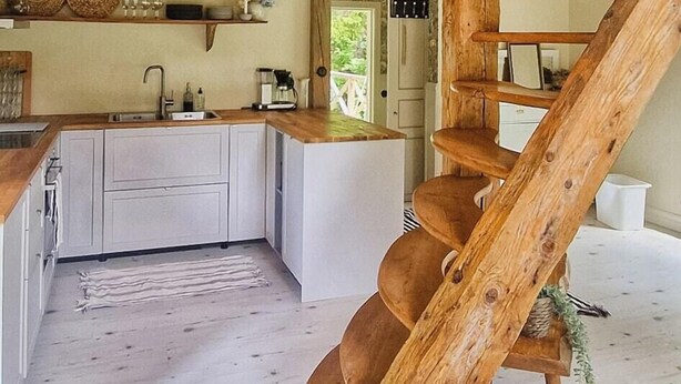 Un interno rustico con una scala in legno, una cucina con mobili bianchi e un soffitto in legno.