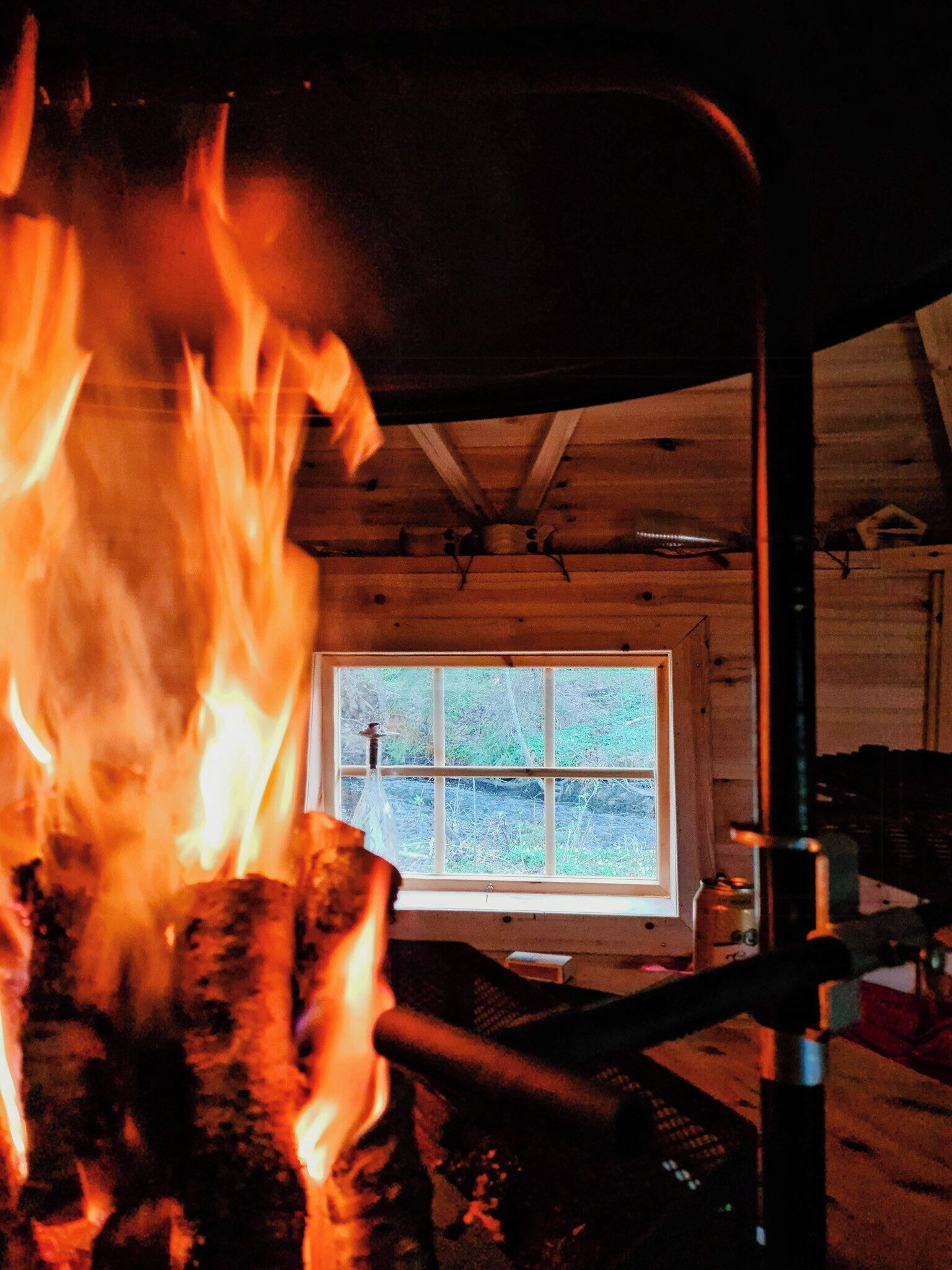 Une pièce avec une fenêtre, un plafond en bois et un feu qui brûle dans un récipient en métal.