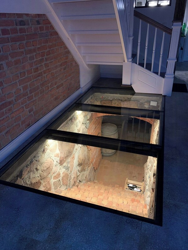 Eine gläserne Konstruktion, die eine Ausgrabungsstätte mit Backsteinmauern und einer Treppe zeigt.
