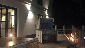 A building with a white exterior, a wicker chair, a small table with a candle, and a fire pit. - Idyllic Country House by the Castle Pond in Gorow (Satow)