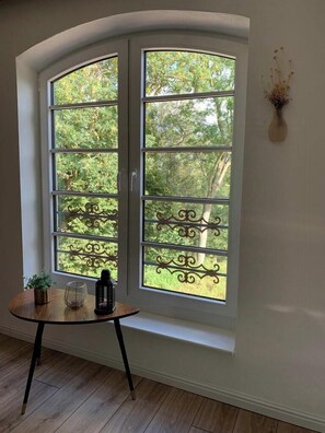 A room with a curved window, a small round table with a plant and a bottle, and a vase with dried flowers on the wall.