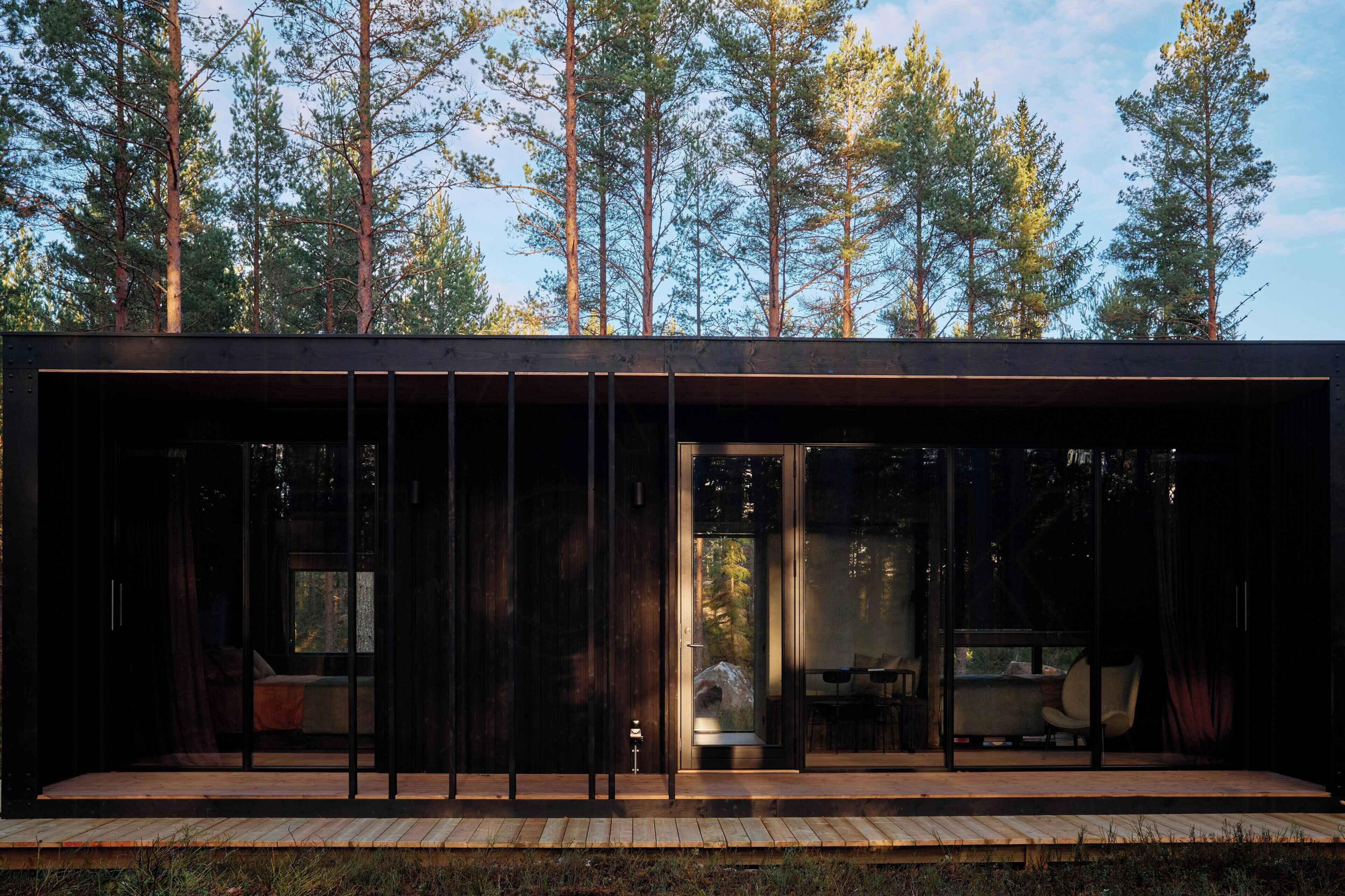 Eine moderne Holzhütte mit Glasfassade, einer Holzdiele und Blick auf hohe Bäume.