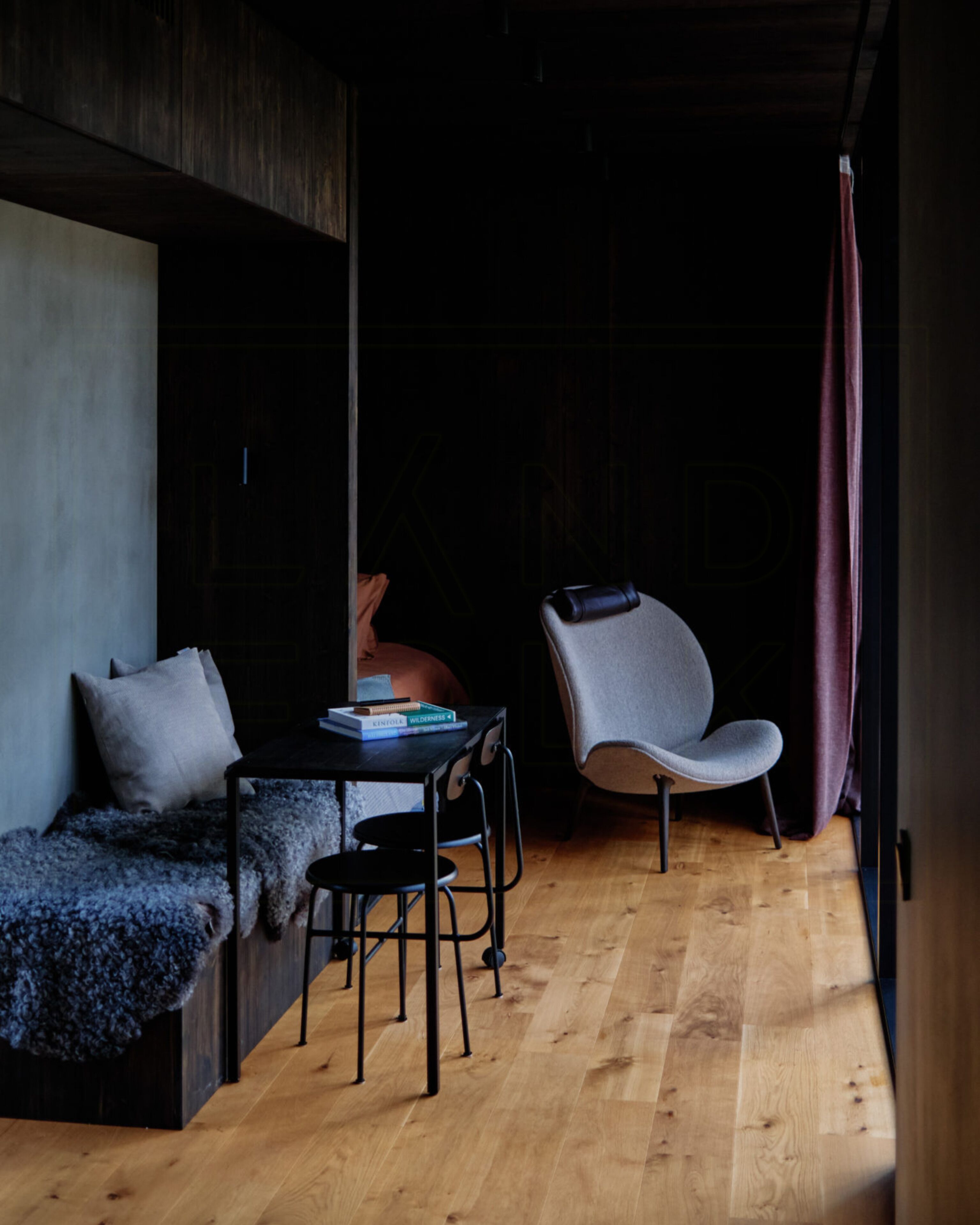 A room with a wooden floor, a black table with chairs, a grey sofa, and a red curtain.