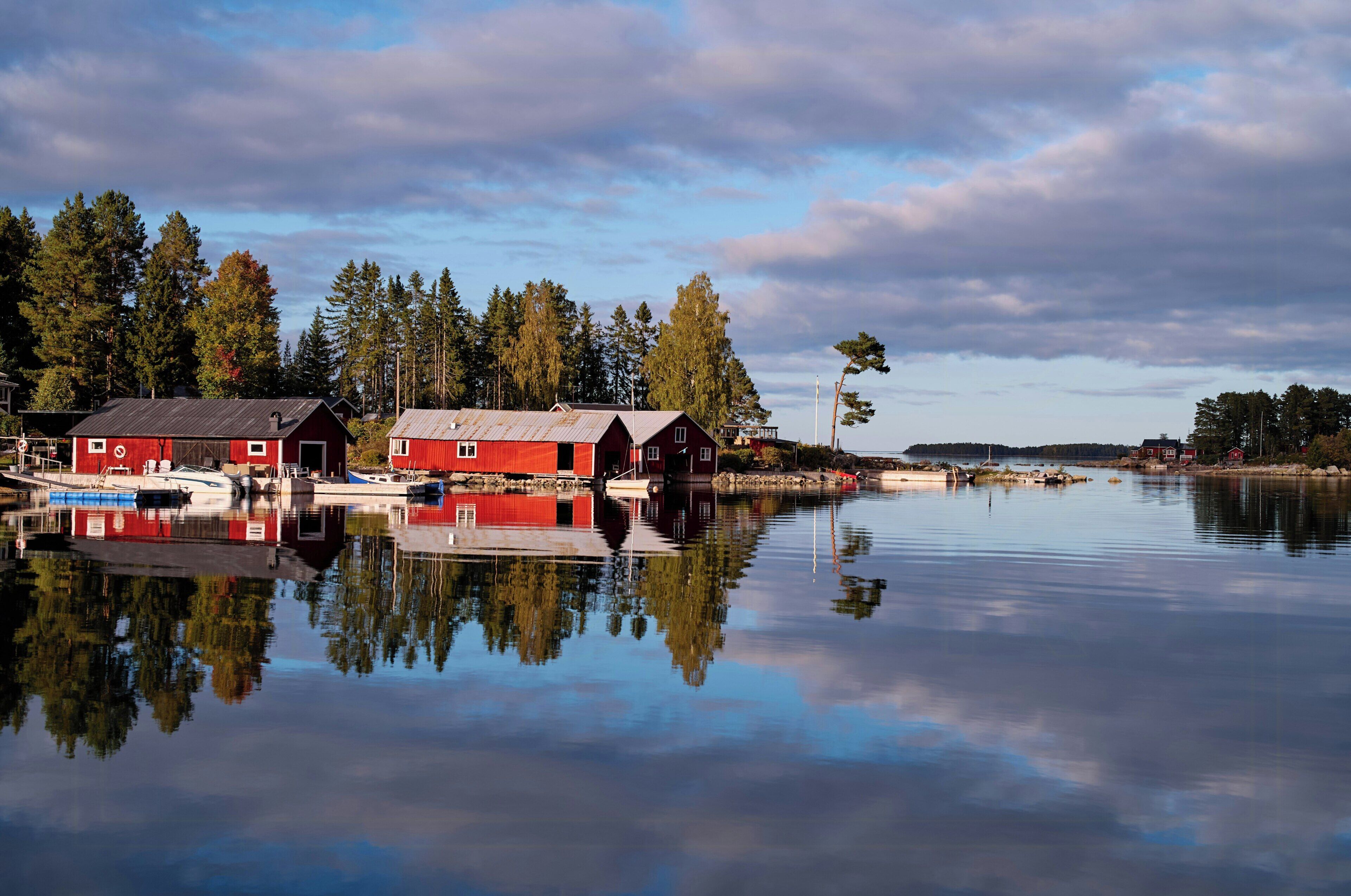 Un lago tranquilo con edificios rojos reflejados en el agua, rodeado de árboles.