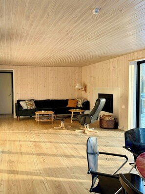 Ein modernes Wohnzimmer mit Holzbalkendecke, einem schwarzen Sofa, einem schwarzen Sessel, einem kleinen runden Tisch und einem Kamin.