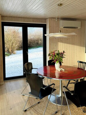 Ein Essbereich mit einem runden Tisch, Stühlen, einer Vase mit Blumen und Blick auf eine verschneite Landschaft durch große Fenster.