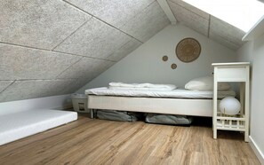 A small, well-lit attic bedroom with a sloped ceiling, a single bed, a bedside table with a lamp, and a shelf with a globe.