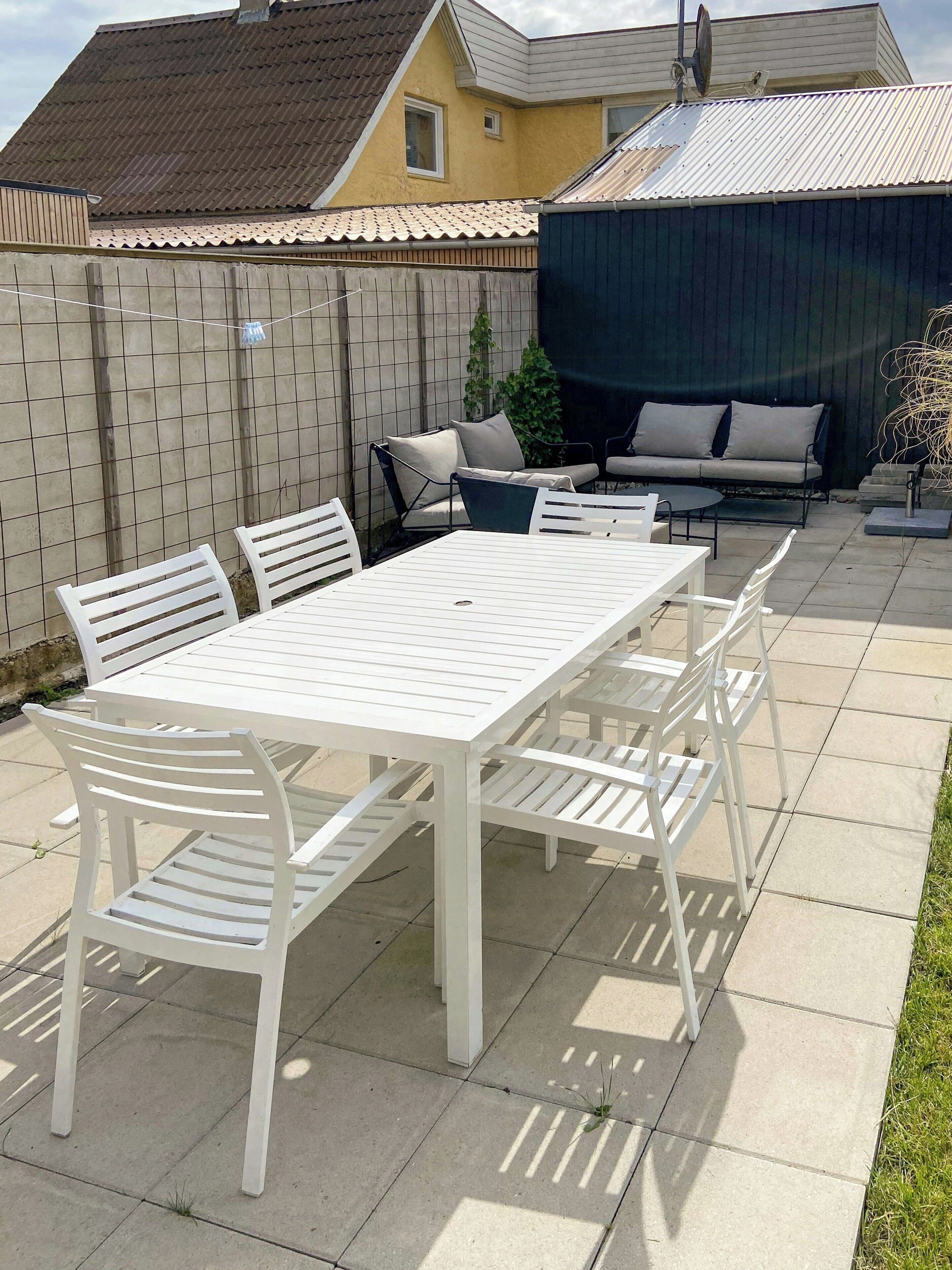 A patio with a white table and chairs, a sofa, and a covered area.