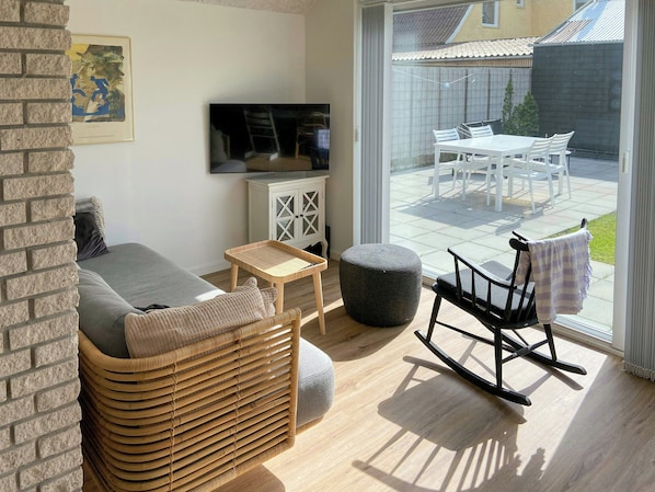A living room with a sofa, a television, a wicker chair, and a view of an outdoor patio.