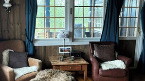 A cozy room with wooden walls, a large window with curtains, a brown leather chair, a wooden coffee table, and a patterned rug.
