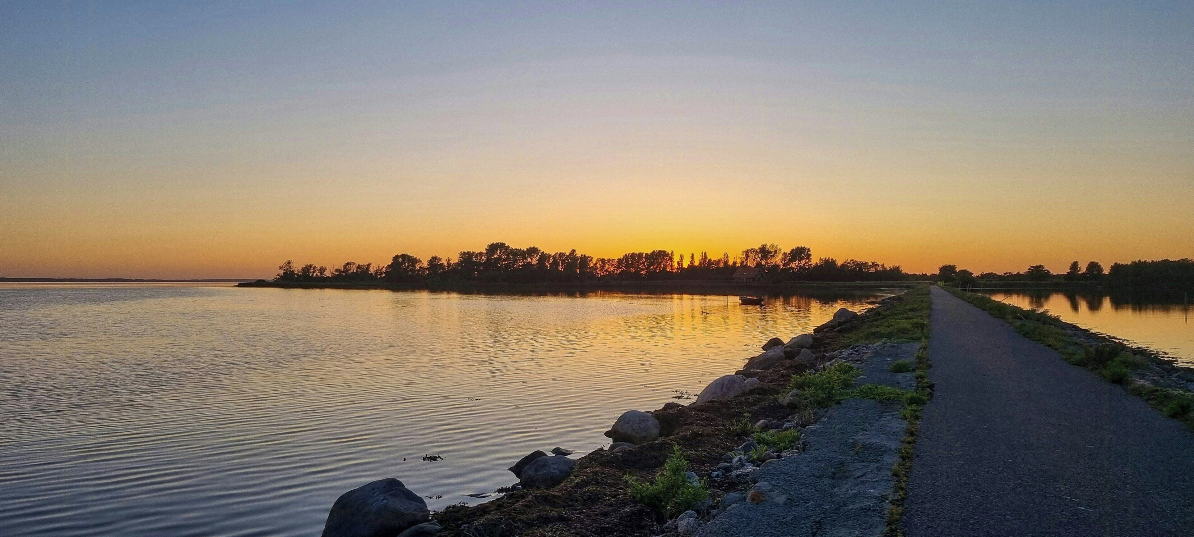 Un lac paisible au coucher du soleil, avec un sentier longeant la rive.