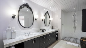 Un baño moderno con dos espejos amplios, encimera de mármol, mueble de tocador negro y zona de ducha.