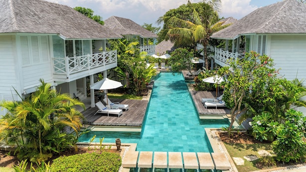 Un resort con piscina central, bungalows sobre el agua y exuberante jardinería tropical.