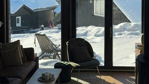 Et værelse med store vinduer, en sofa, en stol og et bord.