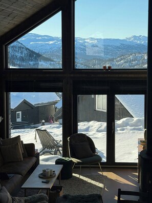 A room with large windows, a sofa, a chair, and a table. - Modern cabin with mountain views in Rauland (Rauland)
