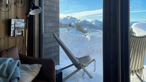 A cozy room with a wooden wall, a window with a view of snow-covered mountains, a chair, and a lamp. - Modern cabin with mountain views in Rauland (Rauland)