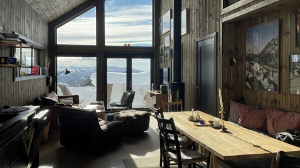 A spacious room with a large window offering a mountain view, a wooden dining table, and a cozy seating area. - Modern cabin with mountain views in Rauland (Rauland)