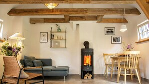 Ein Wohnzimmer mit Sofa, Sessel, Esstisch mit Stühlen, Kamin und Deckenbalken.
