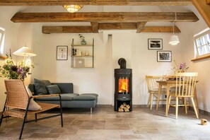 Ein Wohnzimmer mit Sofa, Sessel, Esstisch mit Stühlen, Kamin und Deckenbalken.