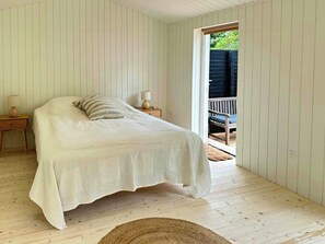 Ein Schlafzimmer mit Bett, Nachttisch, Lampe und Blick auf eine Terrass.