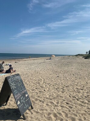 Ein Strand mit einer Kreidetafel, sandigem Gelände und blauem Himmel.