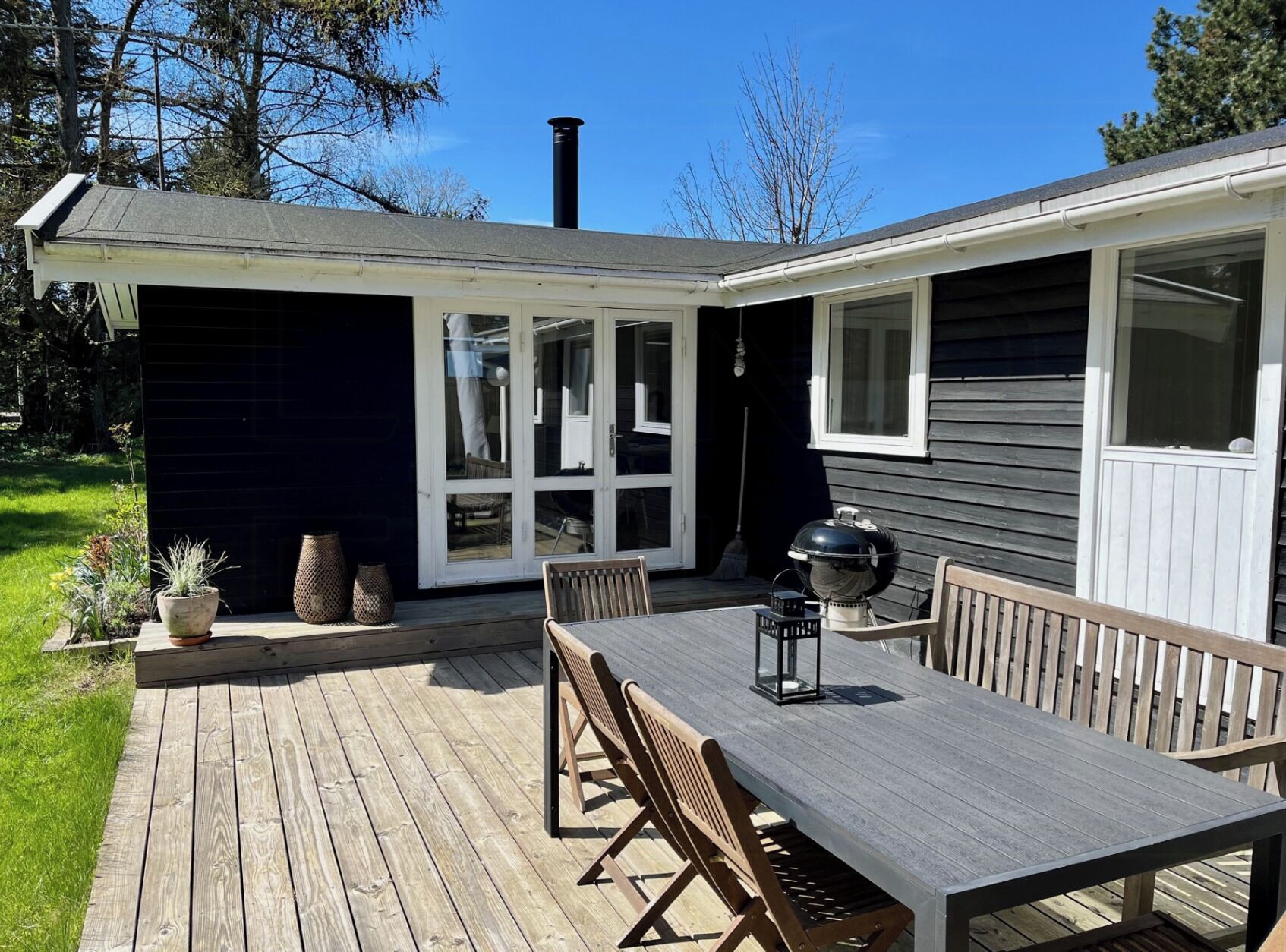 Une terrasse avec une table et des chaises, un barbecue et une maison avec une cheminée.