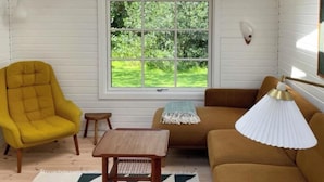 A room with a skylight, a large window with a view of greenery, a yellow armchair, a brown sofa, and a small wooden table. - Elegant summer house close to the beach and forest (Kalundborg)