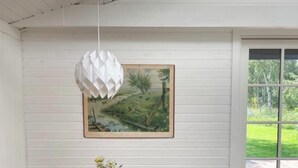 A dining area with a wooden table and chairs, a hanging light fixture, a framed painting, and a view through a window. - Elegant summer house close to the beach and forest (Kalundborg)