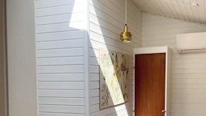 A room with a wooden floor, a woven chair, a small table, a door, and a wall-mounted light fixture. - Elegant summer house close to the beach and forest (Kalundborg)