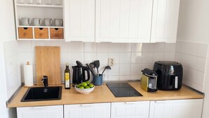 A compact kitchen with white cabinets, a wooden countertop, a sink, a coffee maker, and a bowl of fruit. - Moewennest in Rostock (Rostock)
