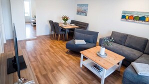 A modern living room with a flat-screen TV, a wooden coffee table, a grey sofa, and a dining area with a table and chairs. - Moewennest in Rostock (Rostock)
