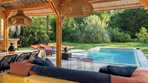 A covered outdoor area with a pool, lounge chairs, and a table with a vase. - American-style villa with pool in Montalivet (Vendays-Montalivet)