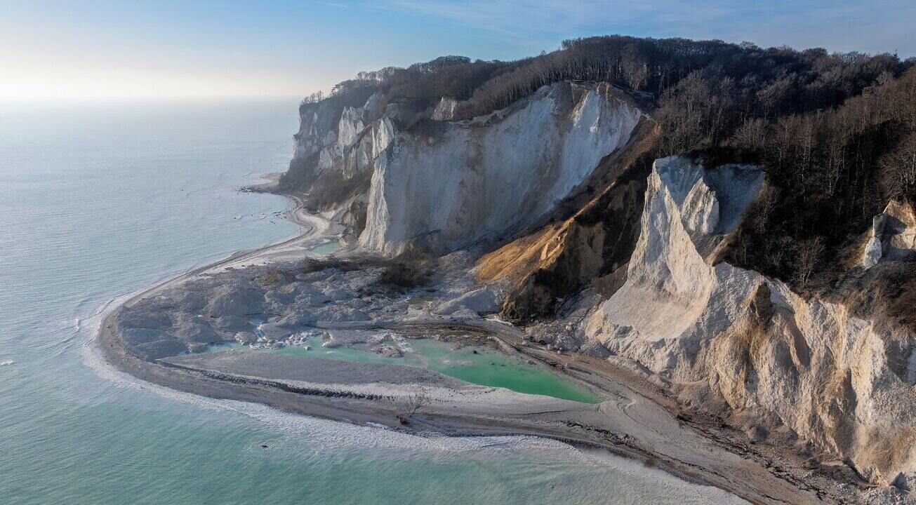 A coastal landscape with cliffs, a beach, and a turquoise lagoon.