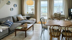 Ein Wohnzimmer mit einer Couch, einem Couchtisch, einem Esstisch, Stühlen und Meerblick durch große Fenster.