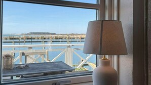 Ein Fenster mit Blick auf einen Steg und Wasser, eine Lampe im Fensterbrett und eine Toilettenpapierrolle.