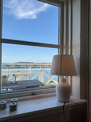 A window with a view of a pier and water, a lamp on the windowsill, and a roll of toilet paper. - Holiday home with harbour view in Klintholm (Borre)