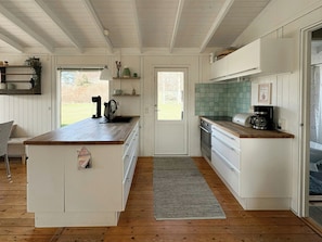 A kitchen with white cabinets, a wooden countertop, a built-in oven, and a coffee maker. - Cozy summer house at Odden (Sjællands Odde)