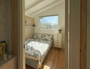 A bedroom with a bed, a dresser, a window, and a shelf with plants. - Cozy summer house at Odden (Sjællands Odde)