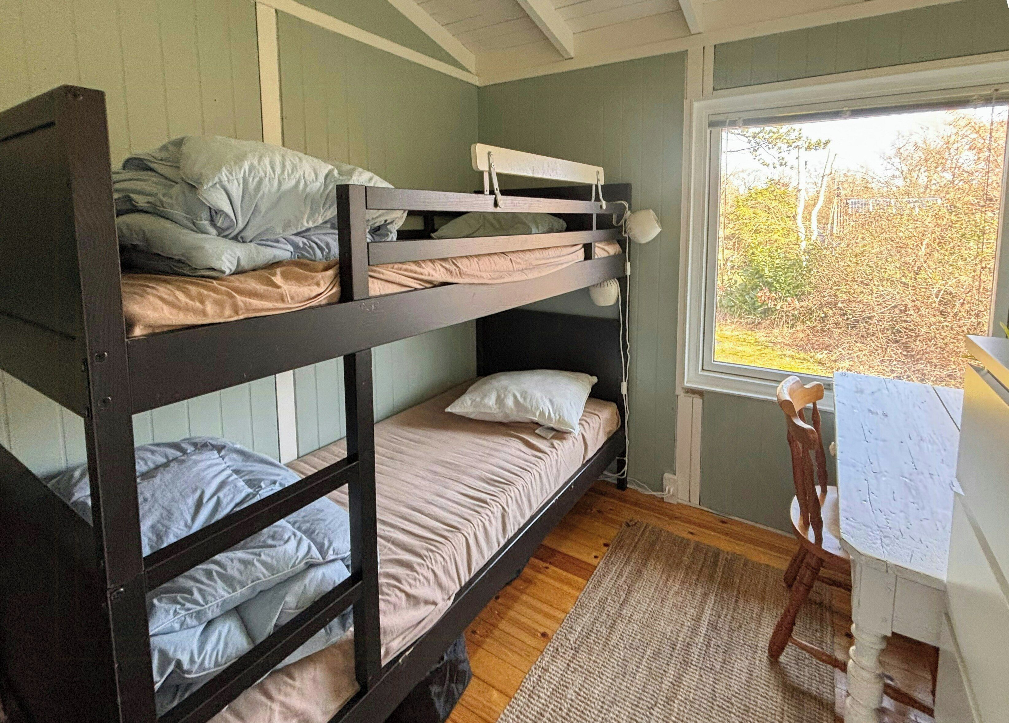 Une chambre avec un lit superposé, un bureau et une chaise, une fenêtre donnant sur des arbres et un plancher en bois.