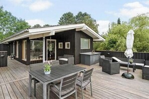 A modern outdoor deck with a dining table and chairs, a small bar area, and outdoor seating. - Cozy summer house at Odden (Sjællands Odde)